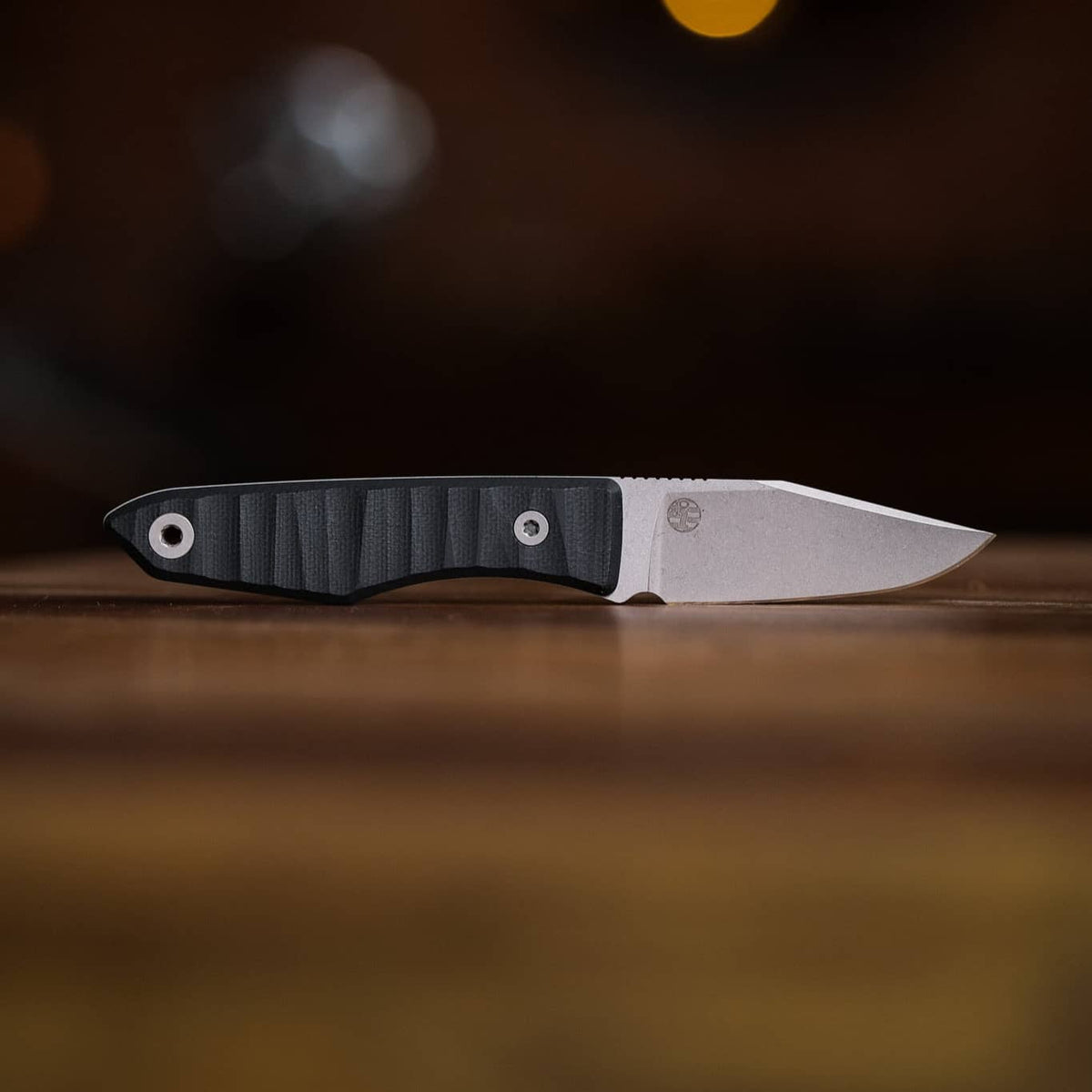 Lookout drop-point knife with dark grooved handle lying horizontally on a wooden table
