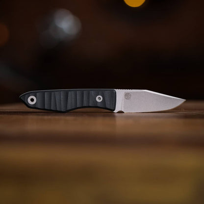 Lookout drop-point knife with dark grooved handle lying horizontally on a wooden table
