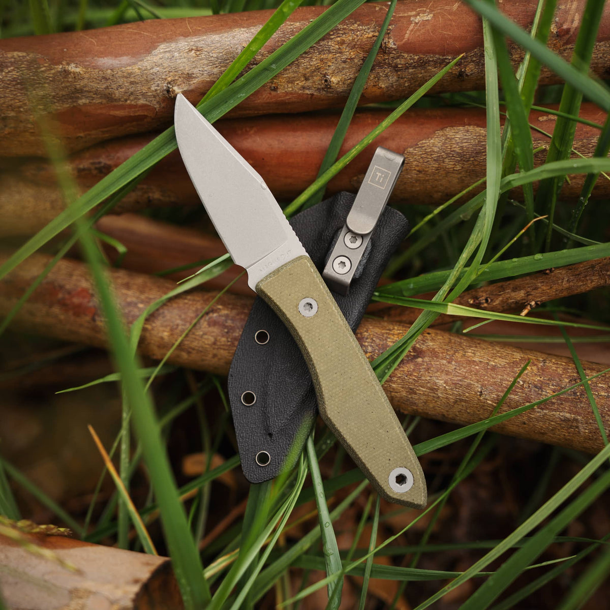 Lookout knife with Green Micarta handle and clipped Kydex sheath resting among branches and grass
