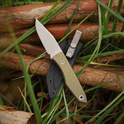 Lookout knife with Green Micarta handle and clipped Kydex sheath resting among branches and grass
