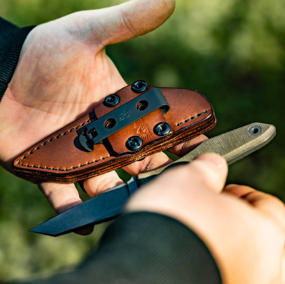Knife and sheath outdoors: Hands holding the Lookout reverse tanto knife and brown leather sheath outdoors