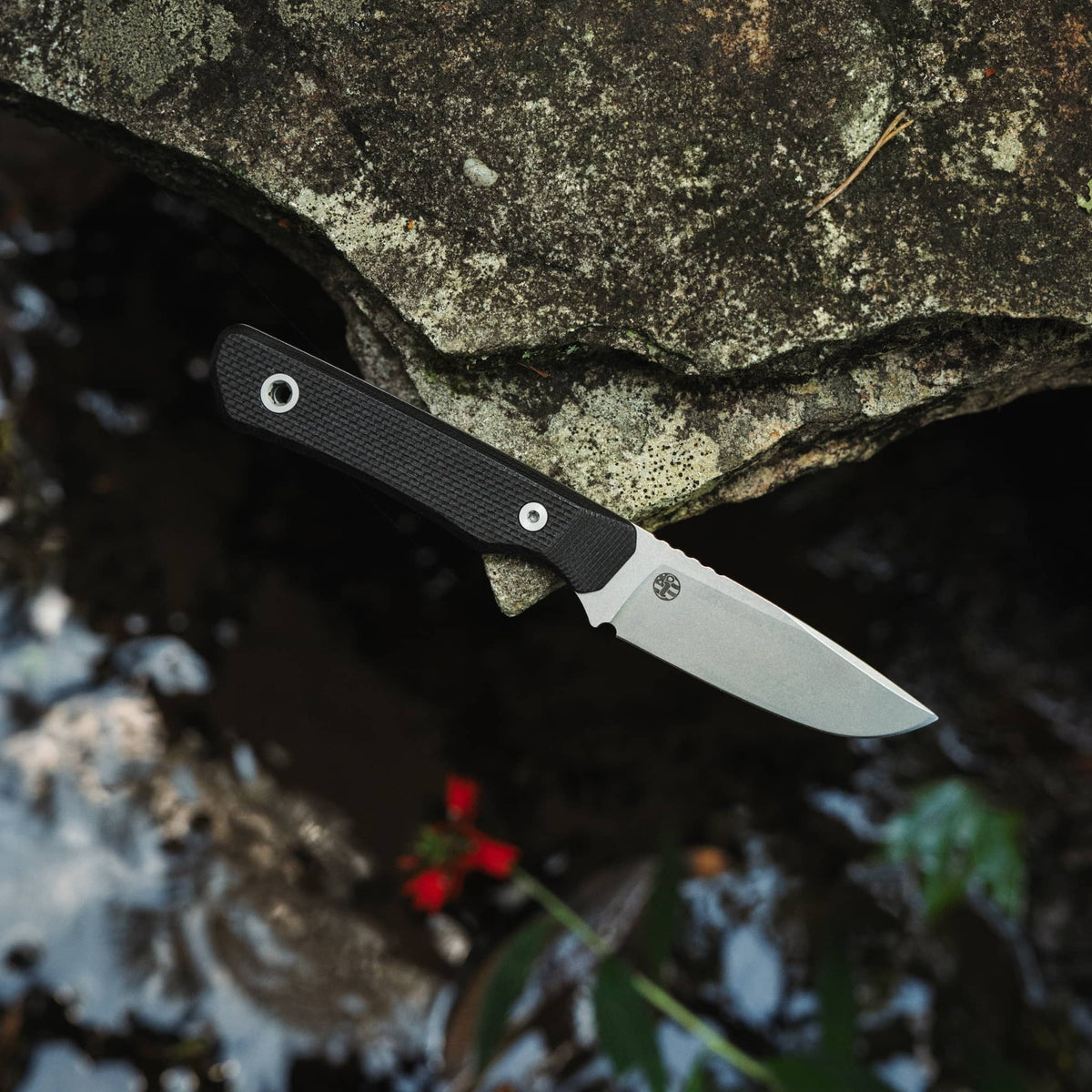 Cloudland MagnaCut knife with Black G10 handle resting on a rock above flowing water