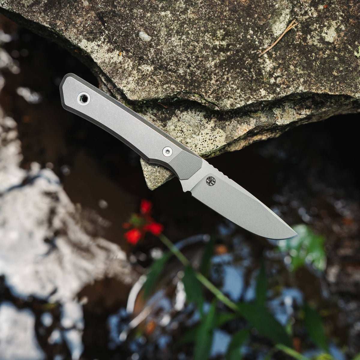 Cloudland MagnaCut knife with titanium handle resting on a rock above a stream