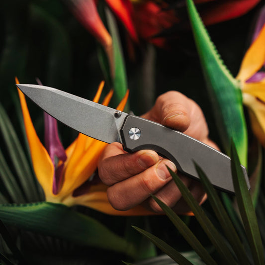 Ti Manu titanium pocket knife held open among bird-of-paradise flowers