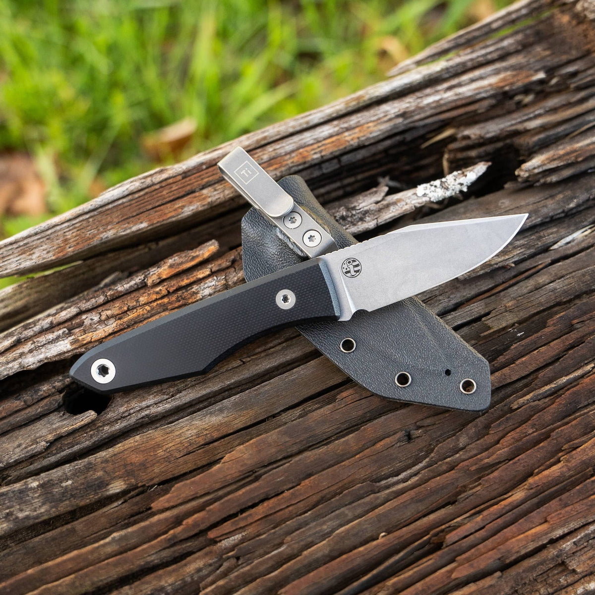 Lookout knife with Black G10 handle and clipped Kydex sheath on weathered wood
