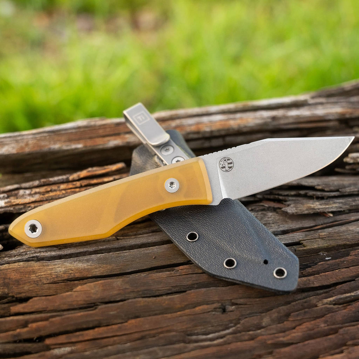 Lookout knife with translucent yellow Ultem handle and Kydex sheath on weathered wood
